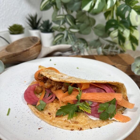 Veganer Taco mit Jackfruit und Kichererbsen, grüner Salsa und frischen Zutaten angerichtet auf einem Teller auf einem Holzbrett